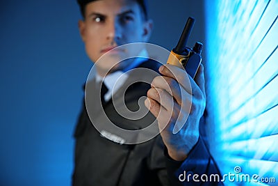 Professional security guard with portable radio set near window in room, focus on hand Stock Photo