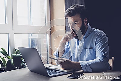 Professional sitting in office in front of laptop. Home-based student getting distant education. Serious man working on desktop Stock Photo