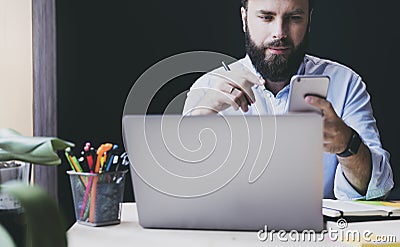 Professional sitting at table in front of laptop, using smartphone. Male person sending text messages, checking email on phone Stock Photo