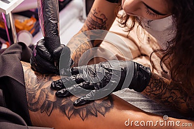 Professional tattooist creating black and white flower design on female thigh Stock Photo