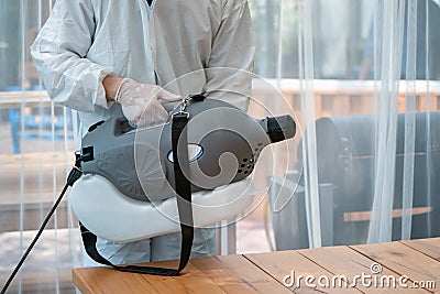 `Professional technical man in prevention suit sprays sterilizing solution.by electrical spray machine in the indoor glass hourse Stock Photo