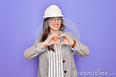 Professional woman engineer wearing industrial safety helmet over pruple background smiling in love showing heart symbol and shape Stock Photo