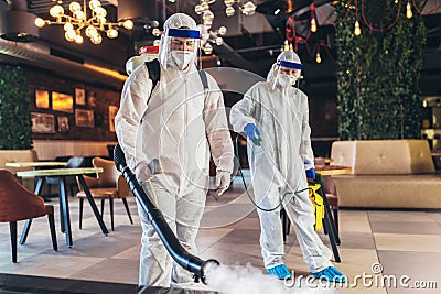 Professional workers in hazmat suits disinfecting indoor of cafe or restaurant, pandemic health risk, coronavirus Stock Photo