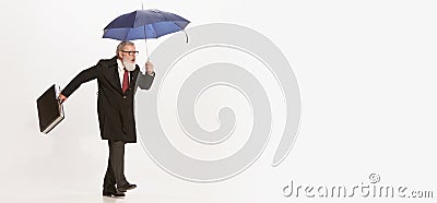 Portrait of active senior man in retro vintage black coat walking with umbrella isolated on white background. Concept of Stock Photo