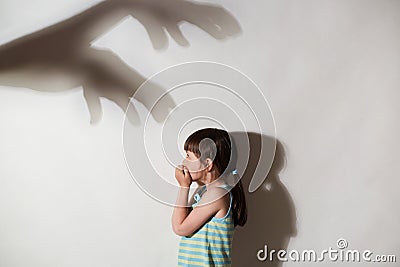 Profile of female kid frightened by the shadows of hands of demons, scared little girl suffering from sciophobia and phantoms, Stock Photo