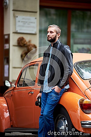 Profile of man leaning on orange retro car. Close-up Stock Photo