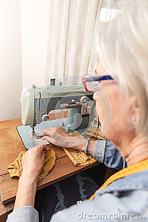 profile of older woman in front of an antique sewing machine cutting a thread from an orange fabric Stock Photo