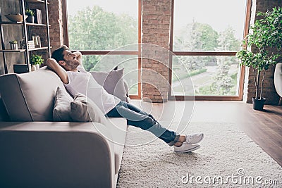 Profile photo of mixed race guy sitting cozy sofa holding hands behind head relaxing homey weekend mood looking dreamy Stock Photo