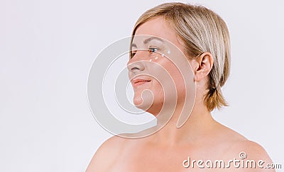 Profile photo. Senior woman with drops of cream under her eyes looks to the side. White background and side advertising Stock Photo