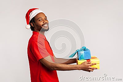 Profile portrait optimistic happy afro-american man with dreadlocks in santa claus hat holding gift boxes looking at camera with Stock Photo