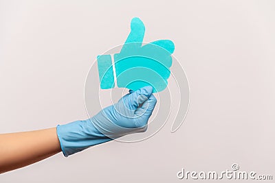 Profile side view closeup of human hand in blue surgical gloves holding and showing like or thumbs up paper shape sign Stock Photo