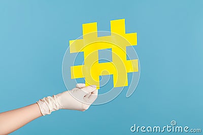 Profile side view closeup of human hand in white surgical gloves holding yellow hashtag Stock Photo