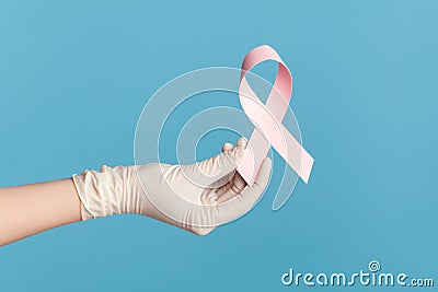 Profile side view closeup of human hand in white surgical gloves shwoing and holding pink ribbon, symbol of breast cancer Stock Photo