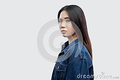 Profile side view portrait of calm serious beautiful brunette asian young woman in casual blue denim jacket with makeup standing Stock Photo