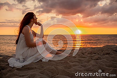 Profile of a single alone or divordes woman silhouette in long white dress sittingon the beach at sunset Stock Photo