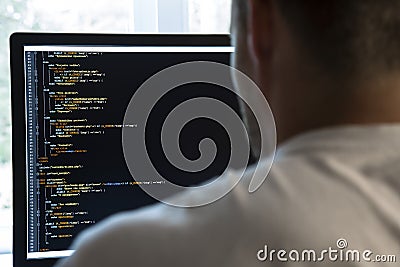 Programmer from behind and programming code on computer monitor Stock Photo