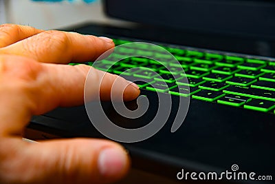 A programmer typing text on a green backlit laptop keyboard Stock Photo