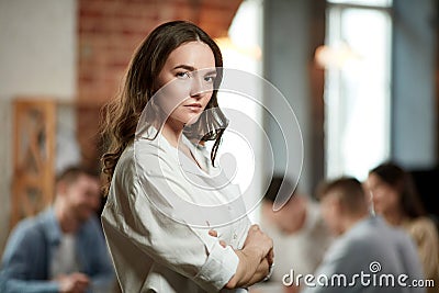 Project manager. Serious ambitious young woman in formal wear attentively looking at camera. Blurred employees on Stock Photo