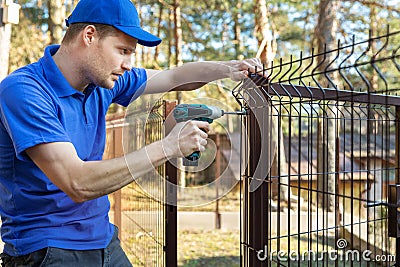 Property territory fencing - man screws metal fence panel Stock Photo