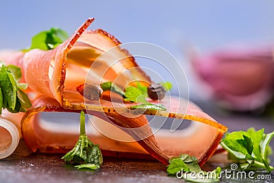 Prosciutto. Curled Slices of Delicious Prosciutto with parsley leaves on granite board. Prosciuto with spice cherry tomatoes Stock Photo