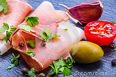 Prosciutto. Curled Slices of Delicious Prosciutto with parsley leaves on granite board. Prosciuto with spice cherry tomatoes Stock Photo