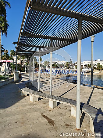 Protaras. Famagusta area. Cyprus. Promenade with a bench and a sunshade, going along the Mediterranean coast to the beach Editorial Stock Photo