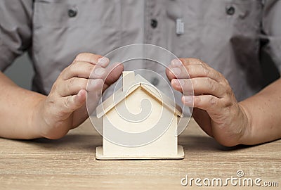 Protection concept, keeping love, male hand guards wooden house on brown table Stock Photo