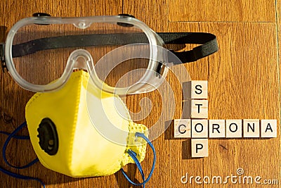 Protective eyewear and yellow mask with outlet valve with wooden blocks spelling out stop corona on a wood floor Stock Photo