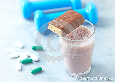 Protein bar, glass of protein shake with milk and raspberries. BCAA amino acids, L - Carnitine capsules and blue dumbbells in back Stock Photo