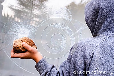 Protester holding a rock to break the glass of a shop window in the street during protests Stock Photo