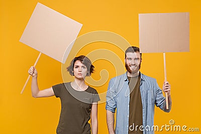 Protesting young two people guy girl hold in hands protest signs broadsheet blank placard on stick isolated on yellow Stock Photo