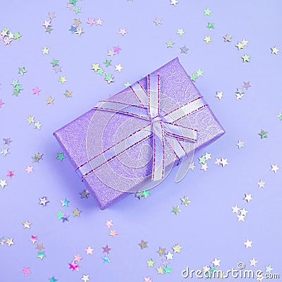 Proton Purple gift box with ribbon and rainbow holographic stars confetti on violet pastel background Stock Photo