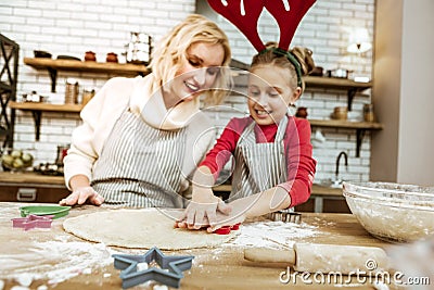 Proud entertained mother in striped apron controlling her daughter Stock Photo