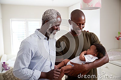 Proud Grandfather With Adult Son Cuddling Baby Grandson In Nursery At Home Stock Photo