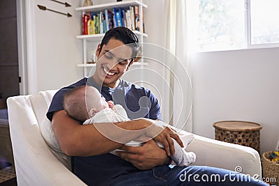 Proud Hispanic father sits holding his four month old son in his arms, horizontal Stock Photo