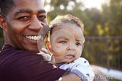 Proud millennial grandfather standing in the garden holding his three month old grandson and smiling to camera, close up, head and Stock Photo