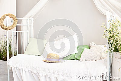 Provence, rustic style. Vase barrel with white daisy flowers in a bright, cozy bedroom interior. White wall, retro bed, straw hat. Stock Photo