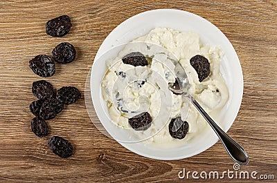Prunes, plate with mix of cottage cheese, sour cream, dried plum, spoon on table. Top view Stock Photo