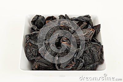 Prunes in white saucer on white background. Top view Stock Photo