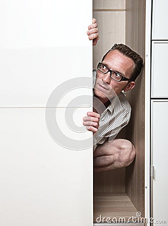 Prying man hiding inside white wardrobe Stock Photo