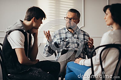 Psychologist talking to depressed teenager and his mum during therapy session Stock Photo