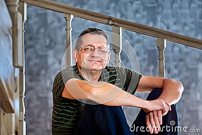 Ptosis of left eyelid in mature European man sitting on an interfloor wooden staircase at home. Stock Photo