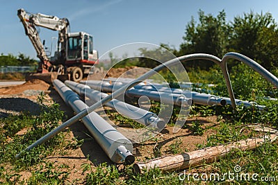 Public lighting poles lying on the ground next to the excavator on the construction site. Stock Photo