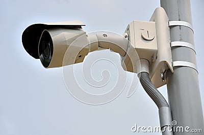 A public surveillance camera installed on a lamp post against a light hazy cloudless blue sky Stock Photo