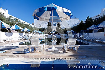 Public swimming pool with sun beds and blue umbrellas Stock Photo