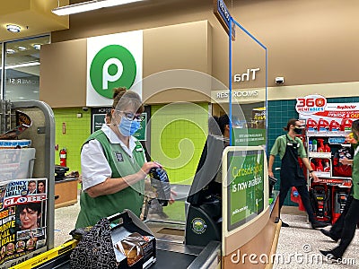 A Publix grocery store employee wearing a face mask and behind a plexiglass shield Editorial Stock Photo