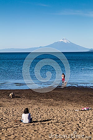 PUERTO VARAS, CHILE - MAR 23: People on a bach of Llanquihue lake in Puerto Varas town. Osorno volcano in the background Editorial Stock Photo
