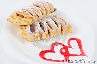 Puff pastry with apples and cinnamon. Delicious dessert with apples and cinnamon. Dessert on a plate with a heart painted jam Stock Photo