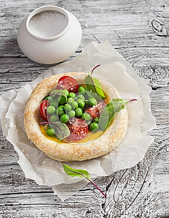 Puff pastry egg tartlet with fresh green peas and cherry tomatoes on wooden rustic board. Stock Photo