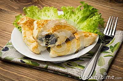 Puff pastry with spinach and feta (triangles) on the wooden background. Stock Photo
